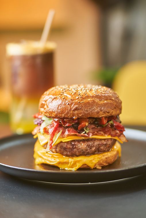 Hamburguesa Manolette’s con cheddar y morrones, junto a un té helado